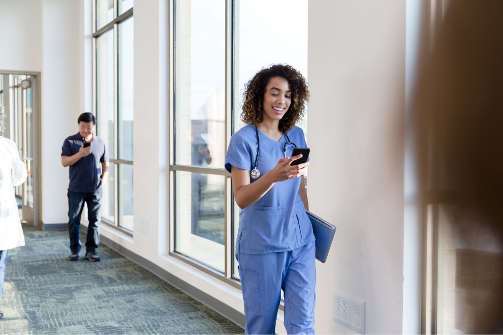 Female nurse walking in a hospital hallway and looking at her phone