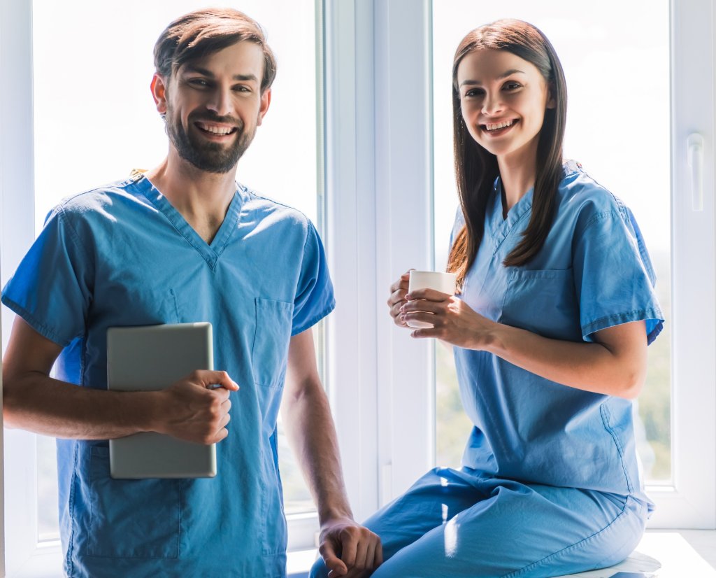 A young nursing couple in scrubs smile for the camera. 
