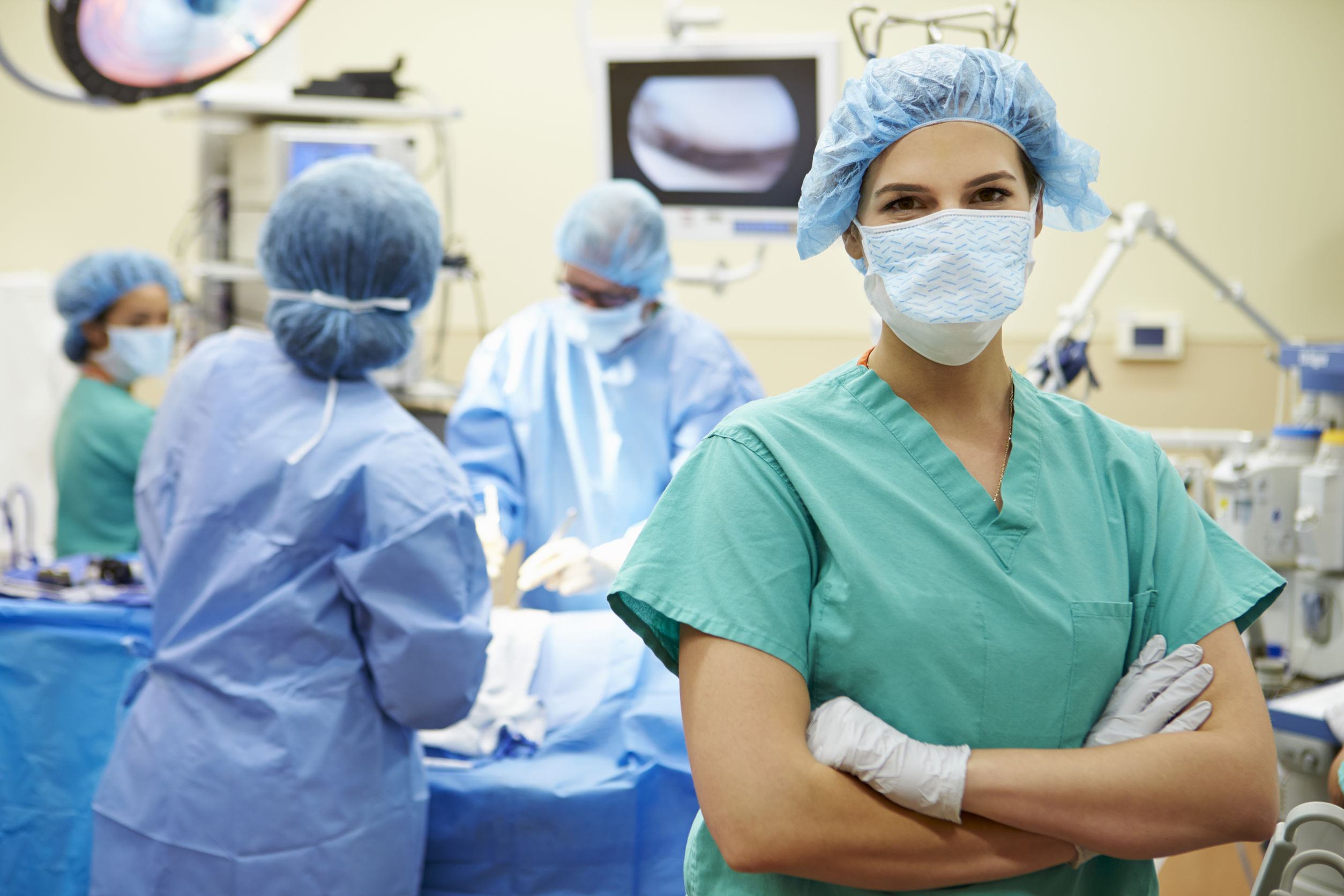 Nurse in operating room surrounded by doctors, arms folded
